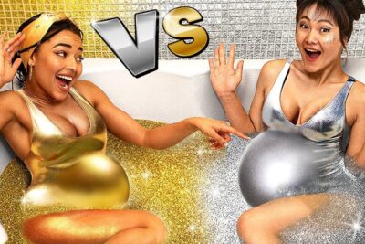 Two glamorous femmes enceintes laughing in a bathtub filled with gold and silver glitter while wearing metallic swimsuits.