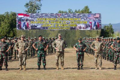 Multinational troop formation standing before a Garuda Shield opening ceremony banner for at 29.