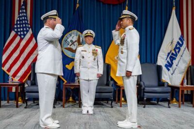 Three naval officers in white dress uniforms salute during a formal change-of-command ceremony for at 34.