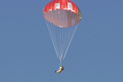 Skydiver descending under a red and white round parachute over a clear blue sky for at 9.