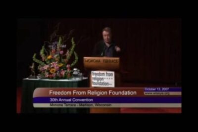 Speaker at a Freedom From Religion Foundation podium for creacionism discussion with floral arrangement on stage