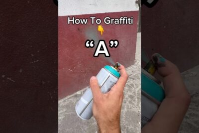 Hand holding a spray paint can aimed at a two-tone exterior wall for graffiti.