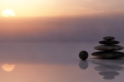 Stacked balancing stones on calm reflective water at sunrise illustrating for och nackdelar med tidsskiftning.