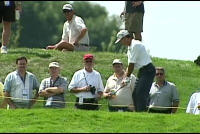 Golfer preparing a measured chip for par 1 with spectators watching from a grassy bank