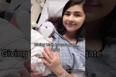Young woman in hospital gown gently cradling a swaddled newborn for surrogatmodraskap