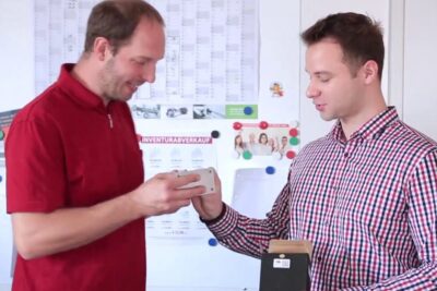 Two colleagues examining a small prototype device in an office setting for forskning utvikling