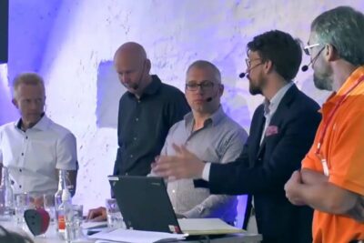 Panel of speakers wearing headsets around a laptop discussing fri handel and trade policy in a conference setting.