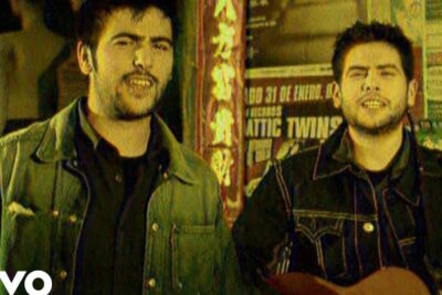 Two musicians in denim jackets singing and playing an acoustic guitar in an urban video scene, fuente energia 1