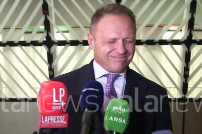 Suit-clad man wincing with eyes closed behind several news microphones during a press moment about geneticamente modificati 1.