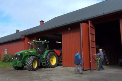 Green tractor outside a large red barn with two people at the open barn door genmodifisert mat 7