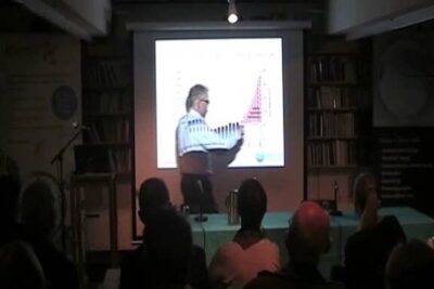 Presenter gesturing at a projected chart during a lecture about genmodifiserte planter.