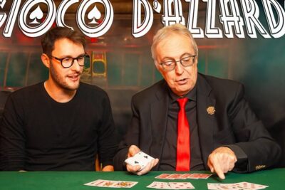 Two men at a green felt casino table demonstrating gioco dazzardo 2 with playing cards laid out