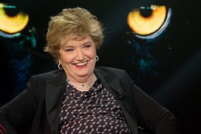 Smiling TV studio guest in front of a dramatic glowing eye backdrop for gioco dazzardo 3.