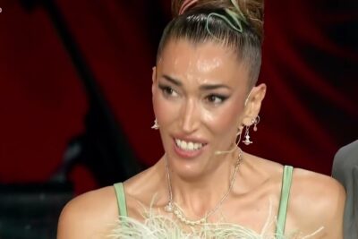 Expressive close-up of a performer in a green feathered dress reacting to giudizio giuria.