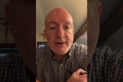 Close-up of a bald man in a checked shirt speaking toward the camera, giustifica mezzi.