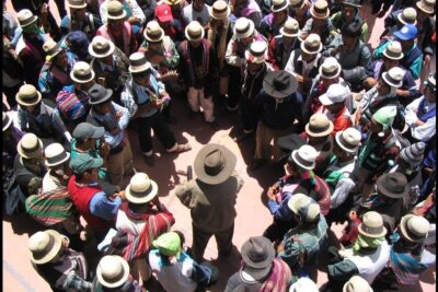 Aerial view of a circular community council of people wearing hats and colorful woven shawls, giustizia indigena 1.