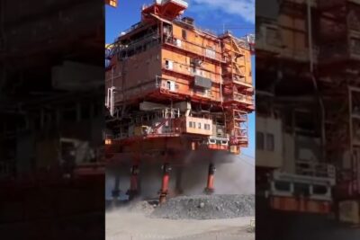 Orange multi-level modular platform raised on hydraulic legs with dust at its base, gruvdrift ar