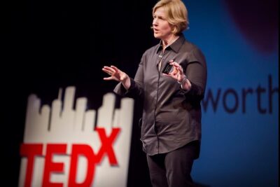 A presenter on a TEDx stage using expressive hand gestures to illustrate handlingar beteenden during a talk.