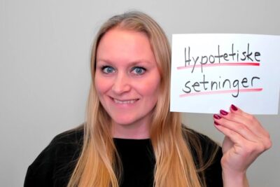 Smiling woman holding a handwritten card mentioning hele satninger