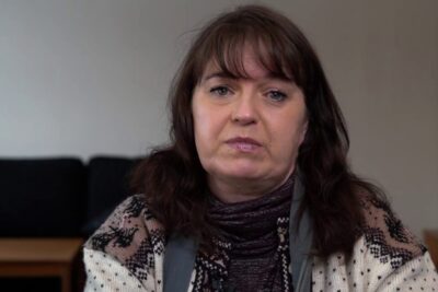 Middle-aged woman seated indoors in a patterned sweater, suitable for henkilokohtaisen kayton.