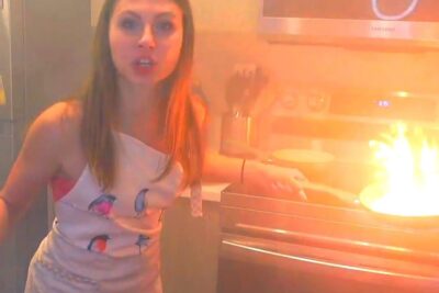 Person in an apron startled by a flaming pan on the stove, showing holdning feil in kitchen posture.