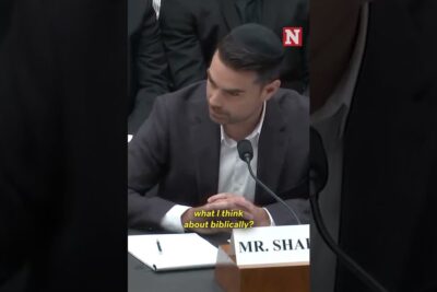 A suited man speaking into a microphone at a formal hearing, homofile par