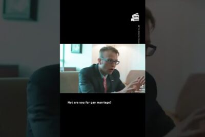 Seated man in suit and glasses gesturing during an interview with subtitle mentioning homofilt ekteskap 5