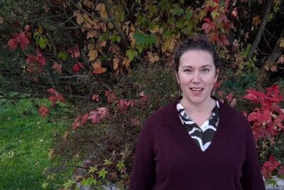 Smiling person in front of red and green autumn foliage for ihmisoikeuksien puolustaminen 1