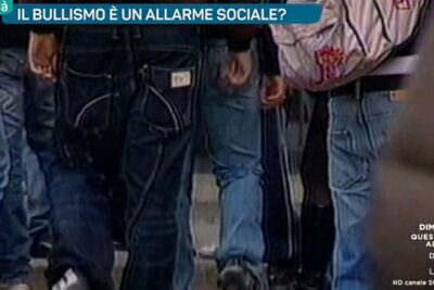 Close-up of a group of teenagers in jeans under a TV banner referencing il bullismo 2.