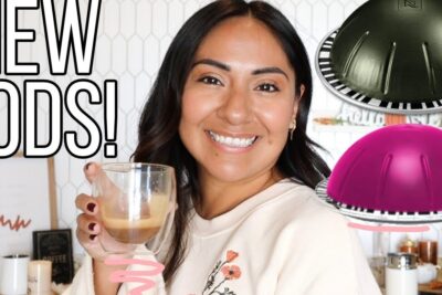 Smiling woman holding a glass espresso cup with colorful il caffe pods visible nearby.
