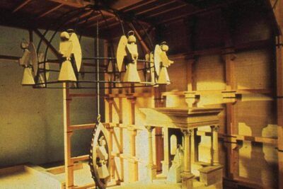 Miniature wooden stage with a ring of suspended angel figures and architectural models evoking il nomadismo.