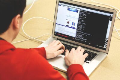 Person typing on a MacBook Pro showing terminal code and a webpage, evoking il velo.