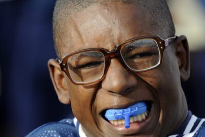 Young football player wearing brown glasses and blue mouthguard in a focused close-up.