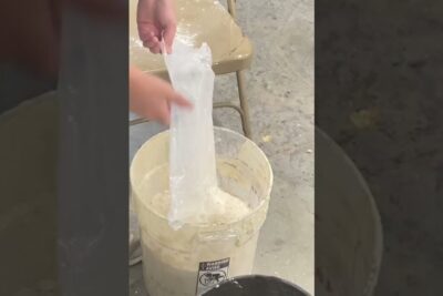 Hands lifting a plastic liner from a bucket of white plaster mix used for imod bornearbejde