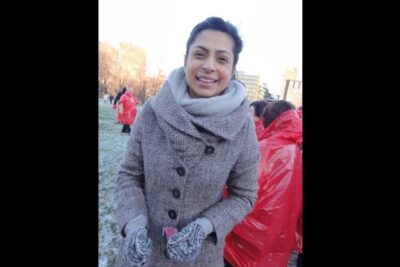 Smiling woman in a grey coat and scarf standing outdoors at an imot atomvapen event