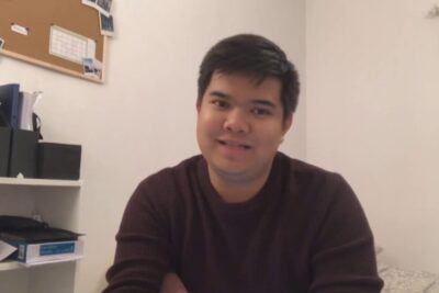 Young man smiling in a casual home office with shelving, documents and a corkboard, industries nationales 1.