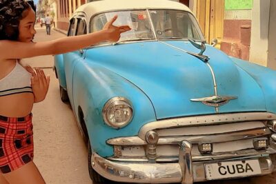 Person gesturing beside a vintage blue Chevrolet with a Cuba license plate illustrating indvirkning pa classic car scene