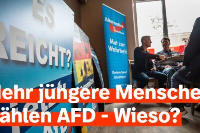A small group of junge menschen and adults sit around a table in a campaign meeting beneath prominent political banners.