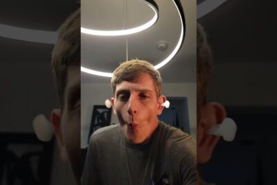 Person making a puckered selfie under a circular jupiter ringer LED halo light while wearing white earbuds.