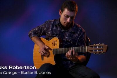 Seated guitarist playing a nylon-string acoustic guitar under blue studio lighting, jus dorange 2.