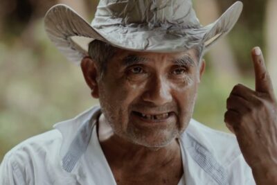 Weathered man in a hat raising a finger in a candid expression, justica indigena 1
