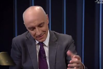 Suit-clad presenter gesturing in a television studio during a discussion about justicia laboral