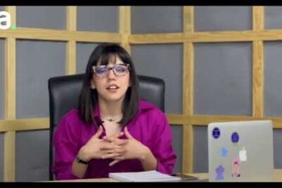 Woman with glasses seated at a desk speaking and gesturing about justicia social 2 during an online presentation