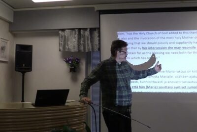 Presenter pointing at projected text about katolisen kirkon 1 during a seminar