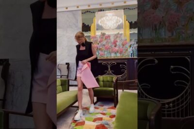 Woman in pink skirt and white chunky sneakers standing in an ornate lounge, kengat laukku