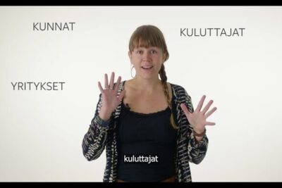 Woman presenter with raised hands against a white background with Finnish words and kestavan kehityksen