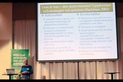 Presenter standing by a projection of a slide about illness experiences and strategies including konsperspektiv ar