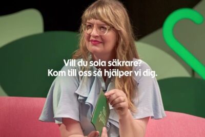 Woman in light blue blouse and glasses holding a green card on a pink sofa with studio backdrop and Swedish overlay text, kontroversiella amnen