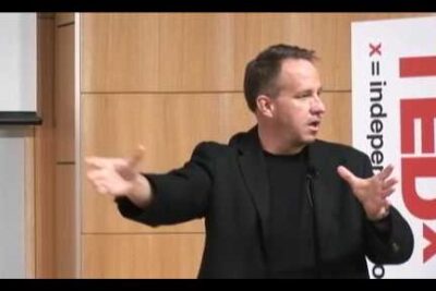 Presenter in a black jacket gesturing broadly on stage at a public talk for kring transhumanism 1.