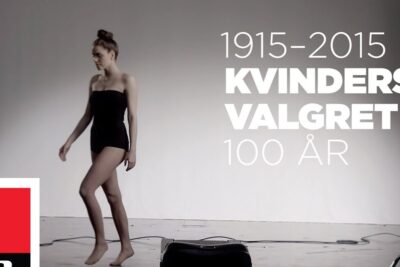 A woman in a black one-piece stands in a photography studio in front of a poster reading kvinders stemmeret 1 and 1915–2015.